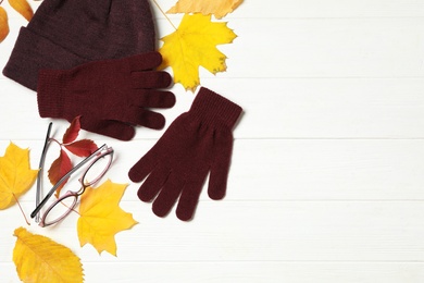 Photo of Flat lay composition with stylish woolen gloves and dry leaves on white wooden table. Space for text