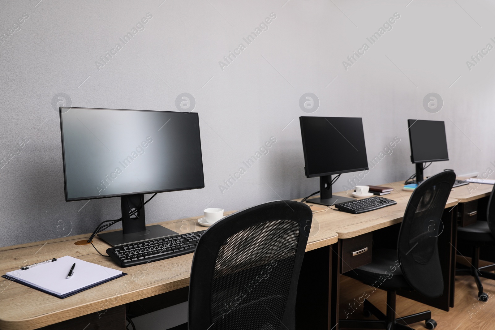 Photo of Open office interior. Modern workplaces with computers near light grey wall