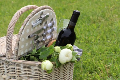 Photo of Picnic basket with wine and flowers on green grass outdoors