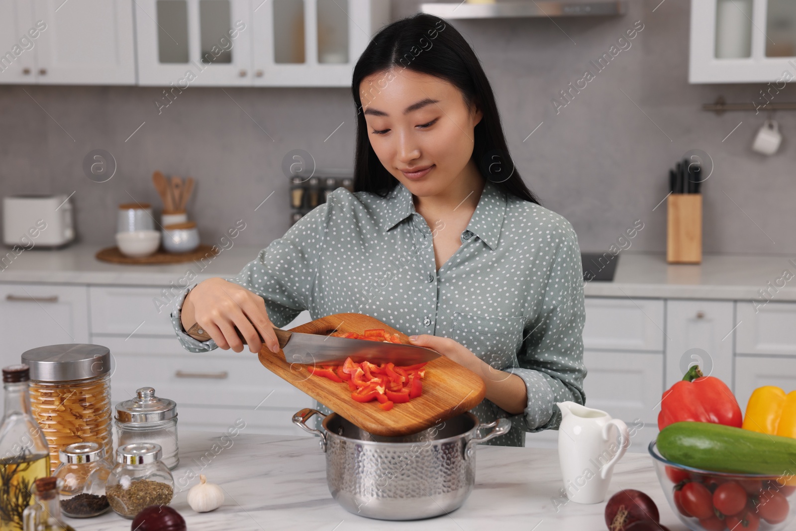 Photo of Cooking process. Beautiful woman adding cut bell pepper into pot in kitchen