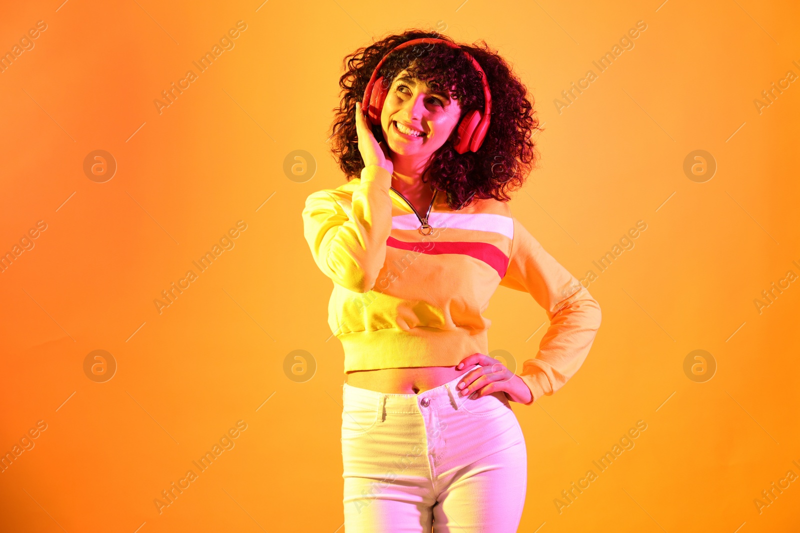 Photo of Beautiful young woman listening to music with headphones on color background in neon lights