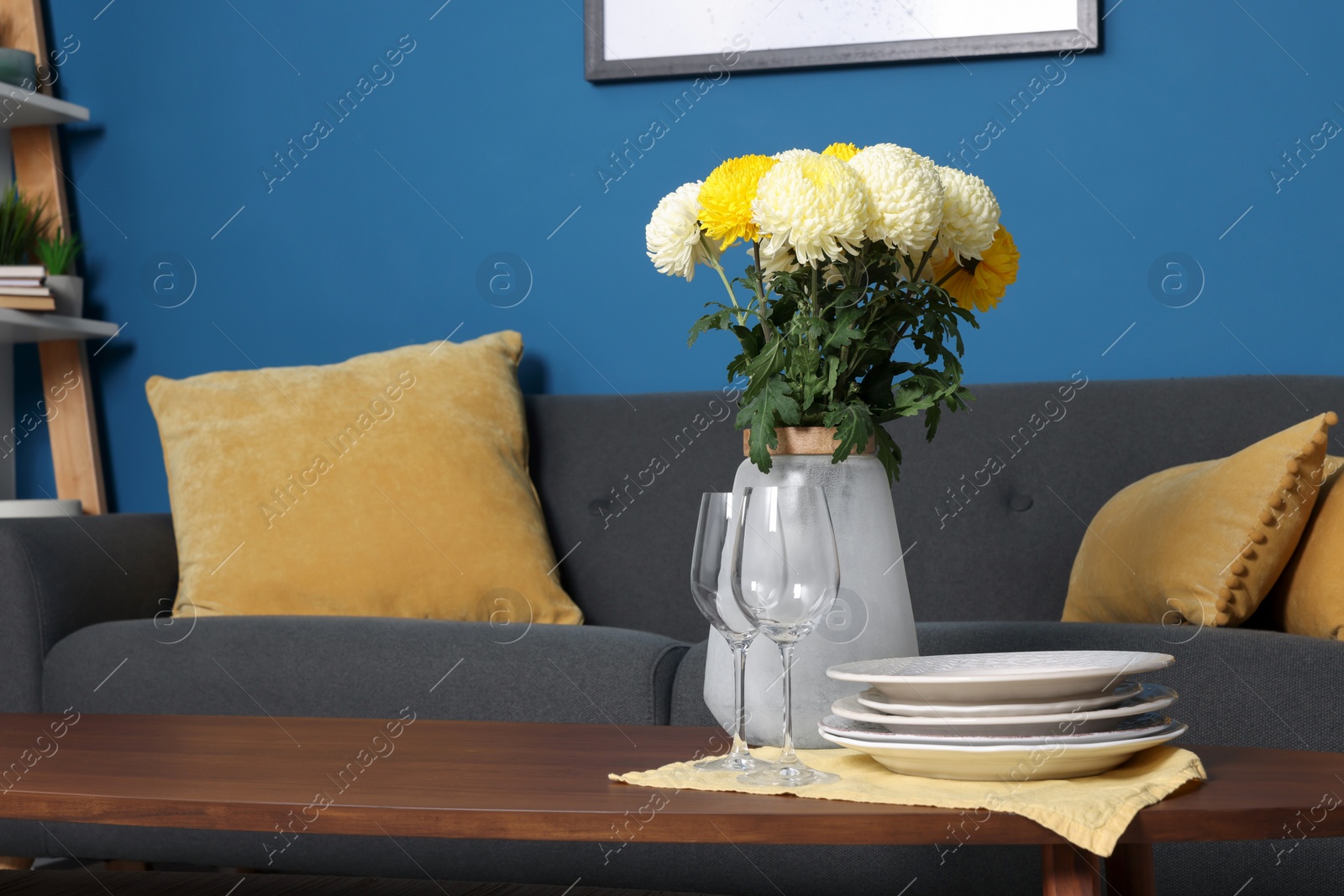 Photo of Vase with beautiful flowers, glasses and plates on wooden table in living room. Interior element