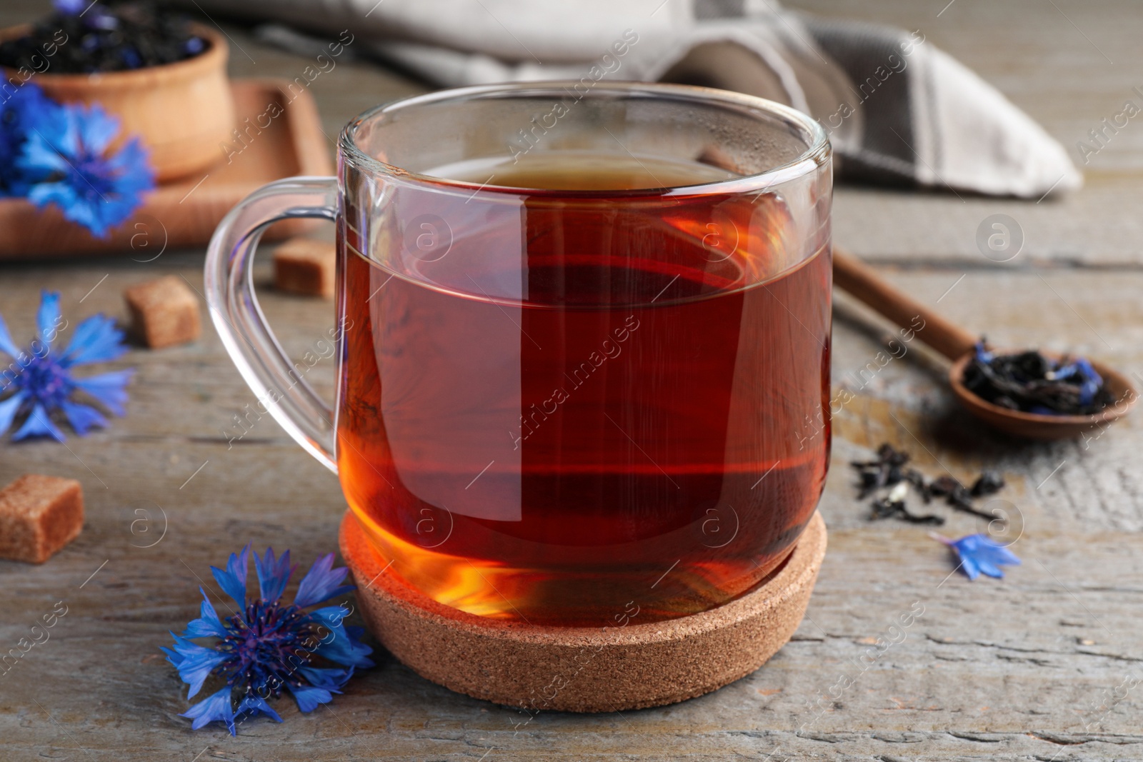 Photo of Glass cup of tea and cornflowers on wooden table, closeup