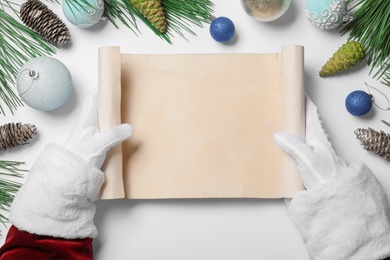 Photo of Santa Claus with blank scroll and Christmas decor on white background, top view. Space for text