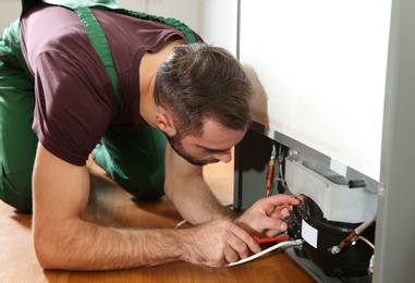 Photo of Male technician in uniform repairing refrigerator indoors