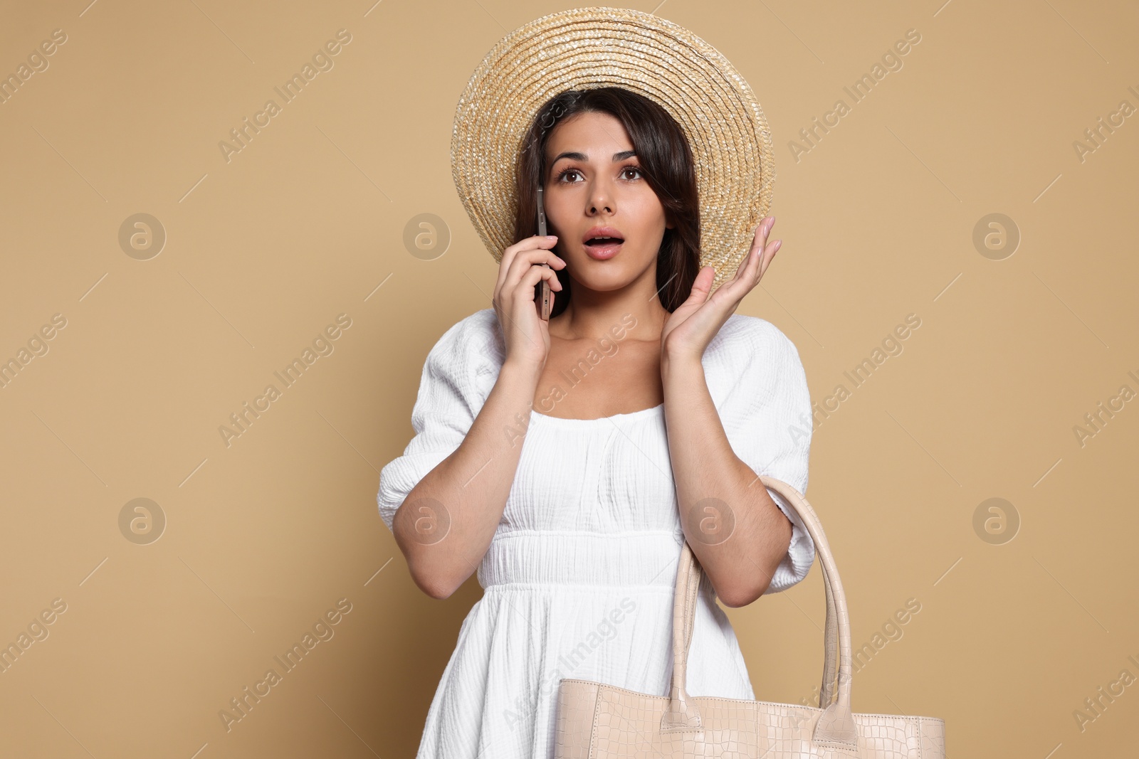 Photo of Young woman with stylish bag and smartphone on beige background