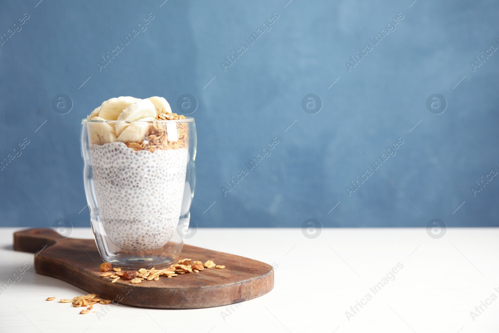 Photo of Glass of tasty chia seed pudding with banana and granola served on table. Space for text