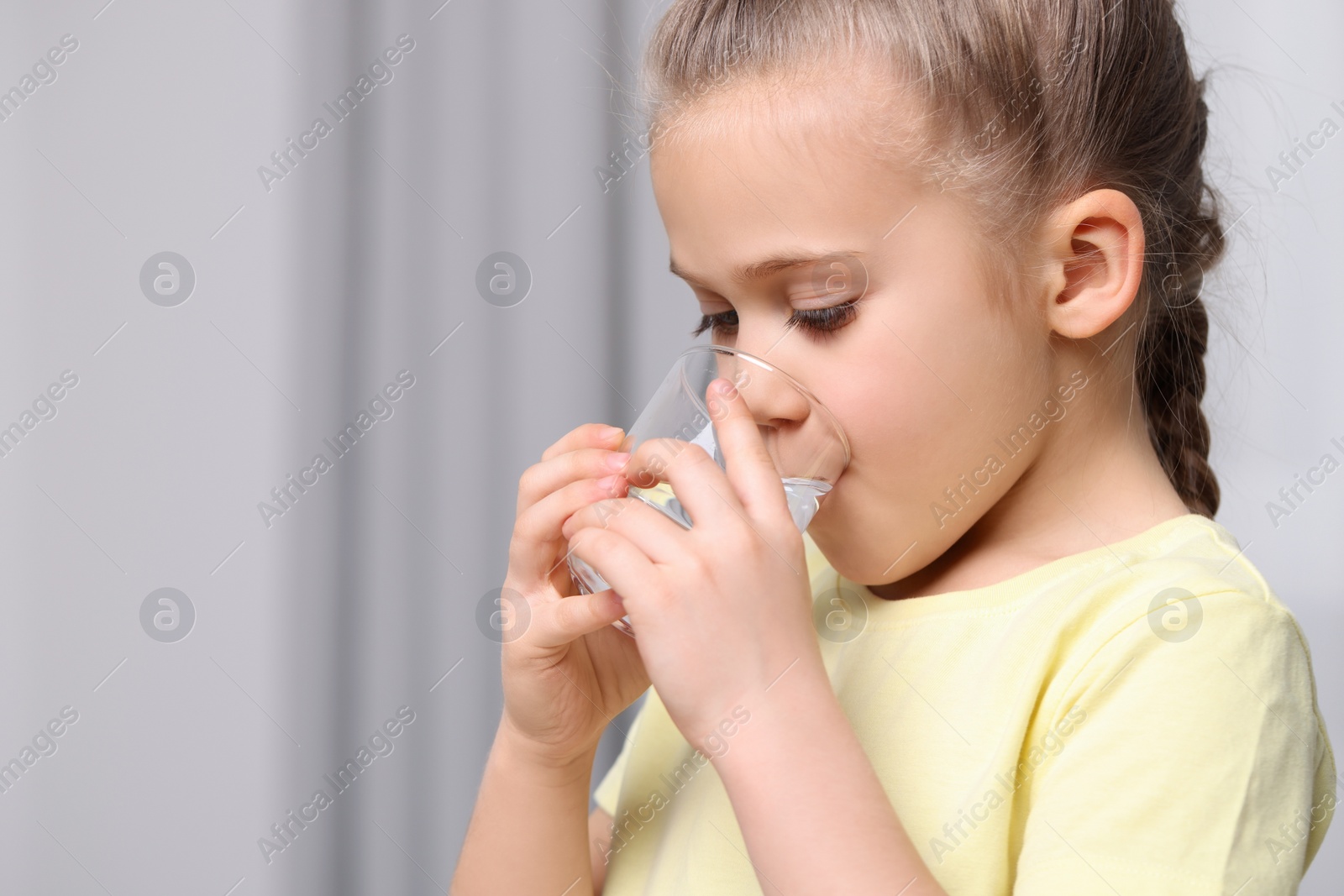 Photo of Cute little girl drinking fresh water from glass indoors