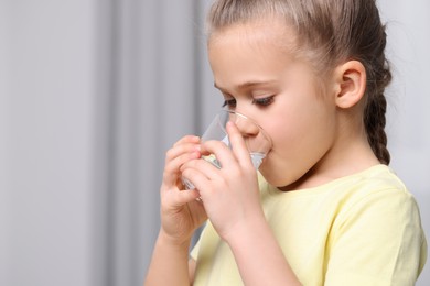 Cute little girl drinking fresh water from glass indoors