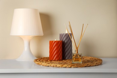 Photo of Aromatic reed air freshener, lamp and candles on white table indoors