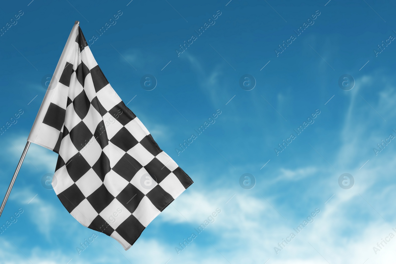 Image of Checkered racing finish flag against blue sky. Space for text