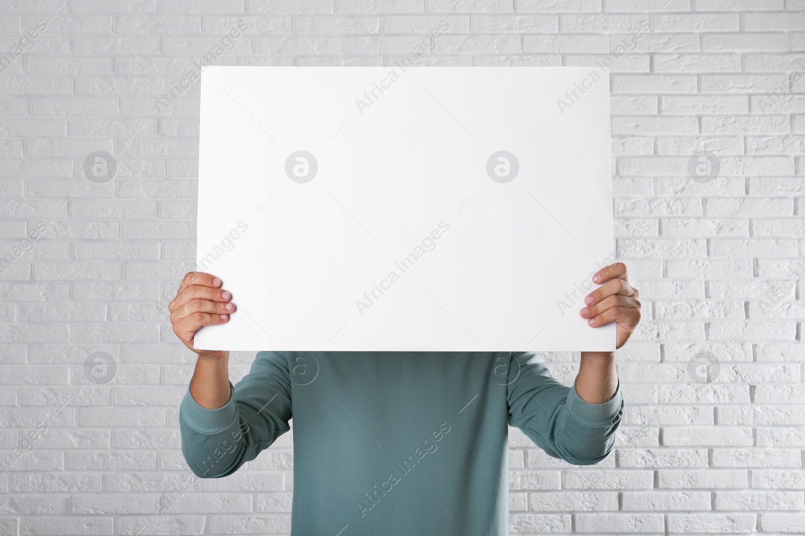 Photo of Man holding blank poster near white brick wall. Mockup for design