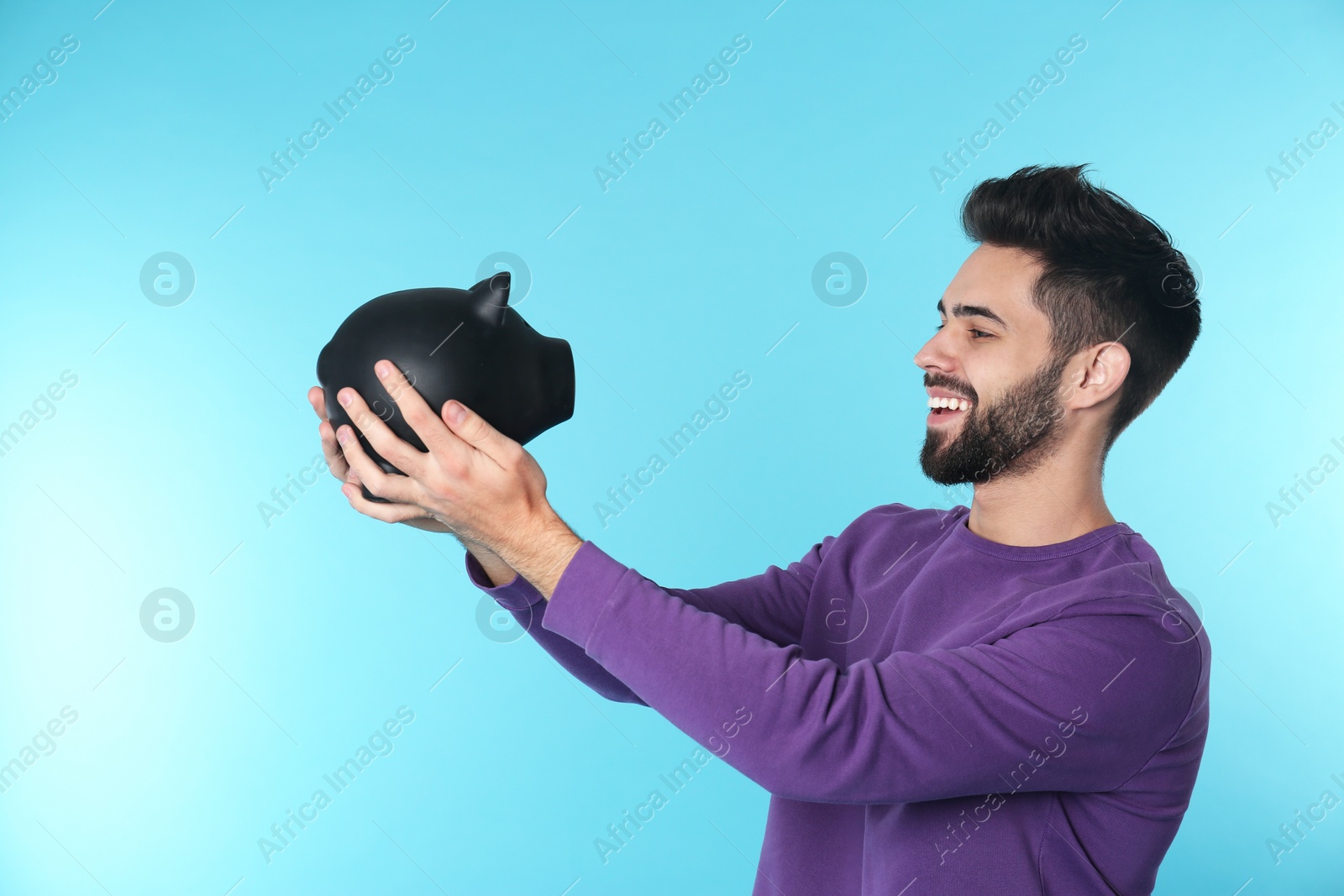 Photo of Happy young man with piggy bank on color background. Money saving