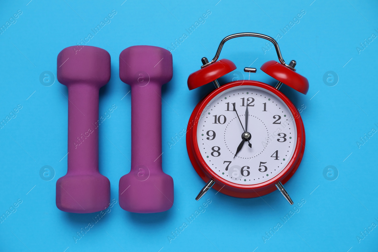 Photo of Alarm clock and dumbbells on light blue background, flat lay. Morning exercise