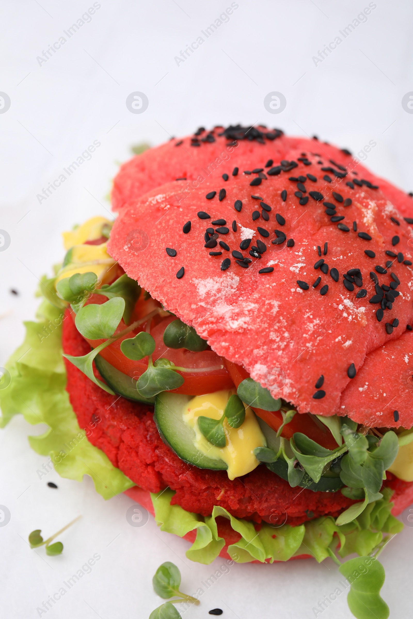 Photo of Tasty pink vegan burger with vegetables, patty and microgreens on white table, closeup