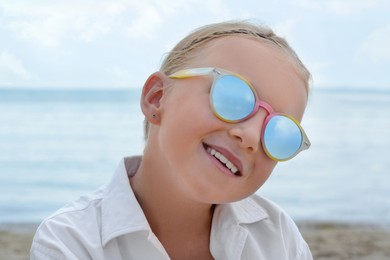 Photo of Little girl wearing sunglasses at beach on sunny day