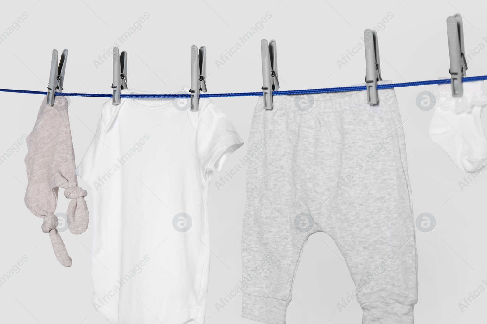 Photo of Different baby clothes drying on laundry line against light background, closeup