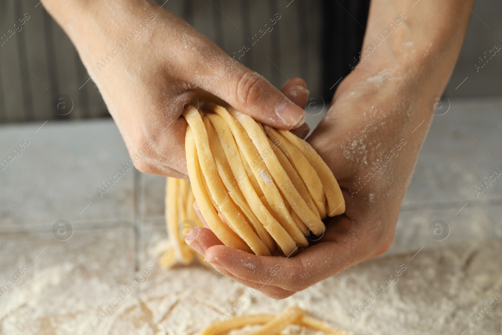 Photo of Woman with homemade pasta at light tiled table, closeup