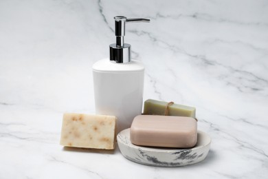 Photo of Soap bars and bottle dispenser on white marble background