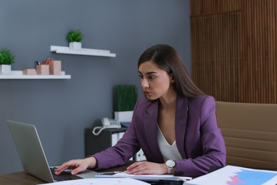 Businesswoman working with laptop and documents at table in office