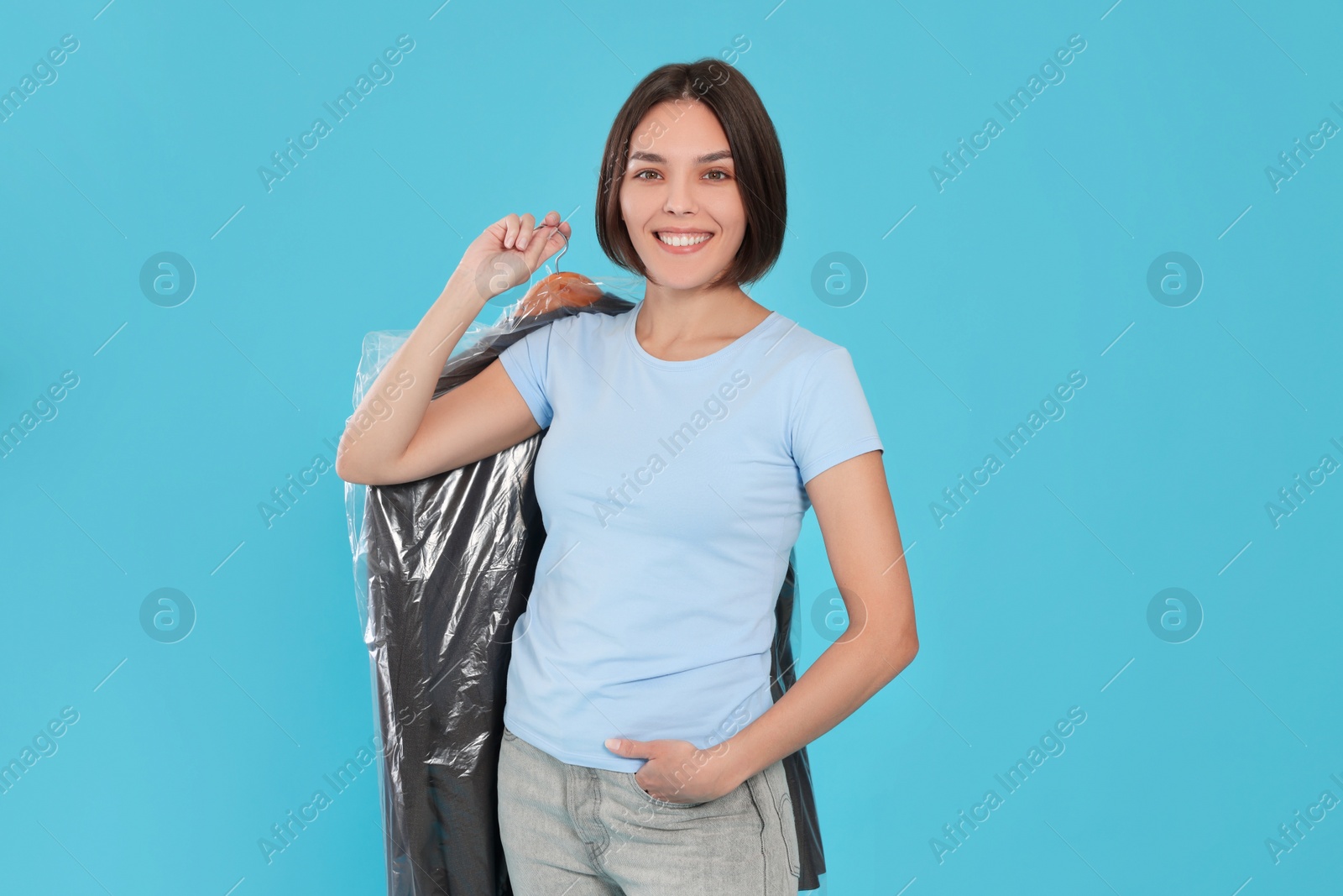 Photo of Woman holding garment cover with clothes on light blue background. Dry-cleaning service