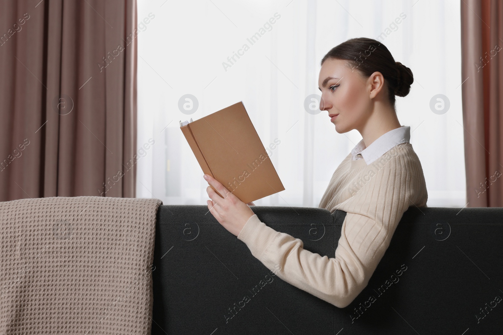 Photo of Woman reading book on sofa near window with stylish curtains at home. Space for text