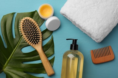 Photo of Hair brush, comb, shampoo, towel and balm on light blue wooden table, flat lay