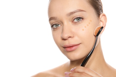 Photo of Young woman applying foundation on her face against white background