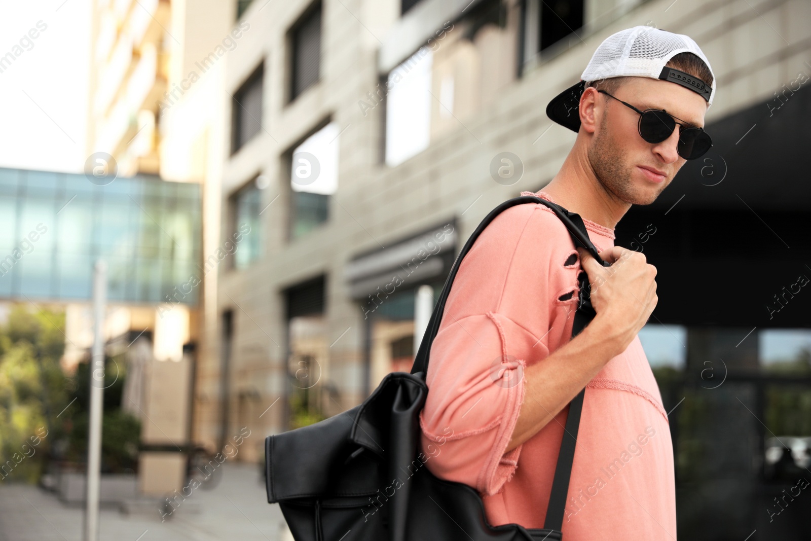 Photo of Handsome young man with stylish sunglasses and backpack on city street, space for text