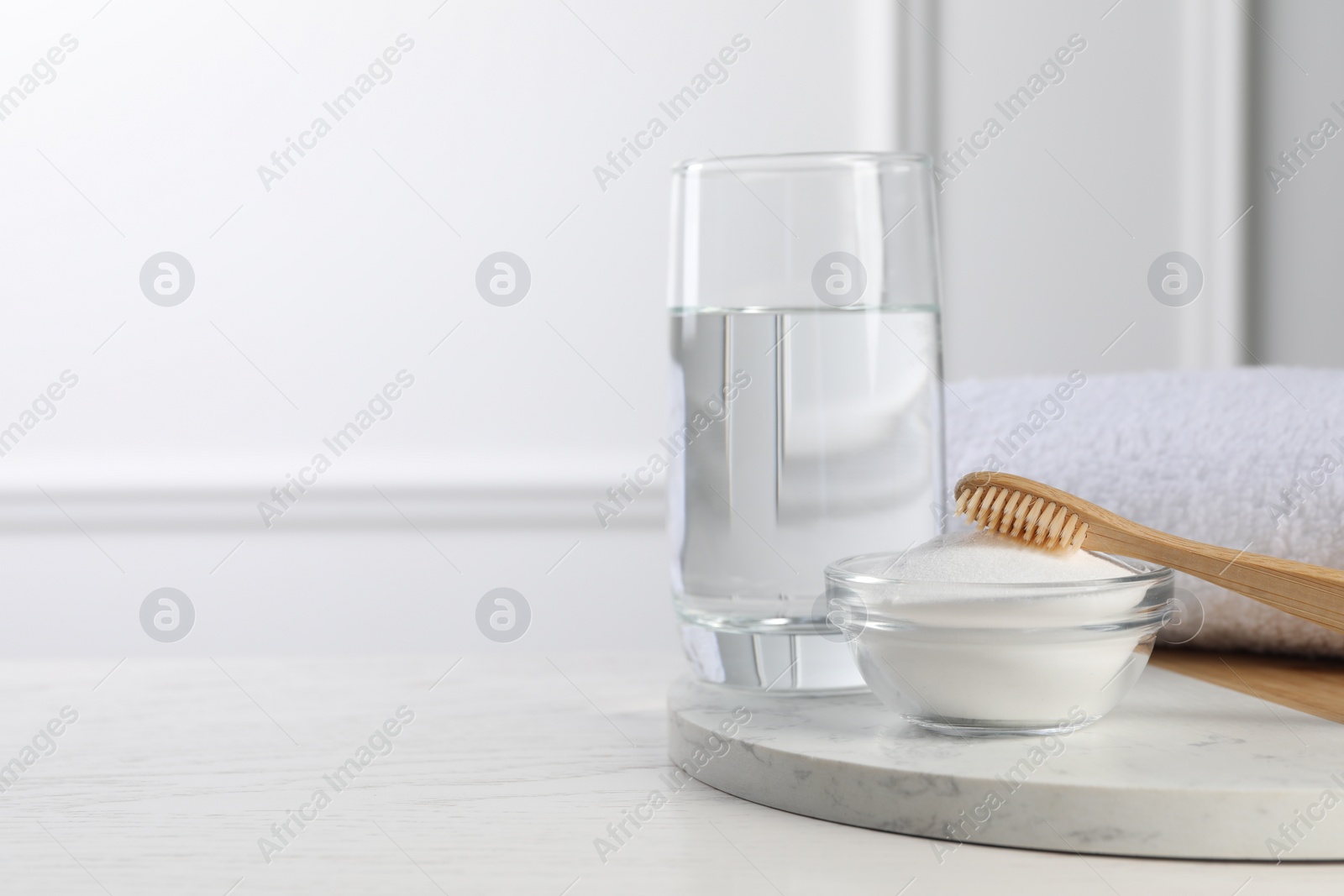 Photo of Bamboo toothbrush, bowl of baking soda and glass of water on white table, space for text