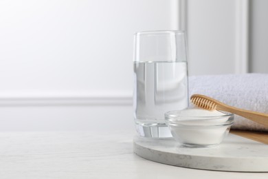 Bamboo toothbrush, bowl of baking soda and glass of water on white table, space for text