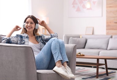 Photo of Young woman with headphones resting in armchair at home