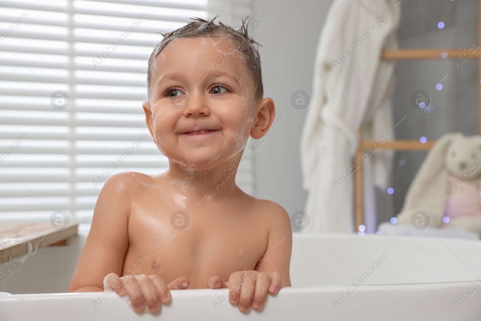 Photo of Cute little boy washing hair with shampoo in bathroom