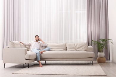 Photo of Man talking smartphone near window with beautiful curtains in living room
