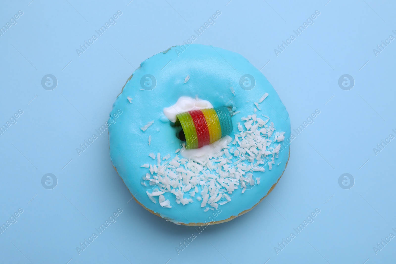 Photo of Tasty glazed donut decorated with coconut shavings and rainbow sour candy on light blue background, top view