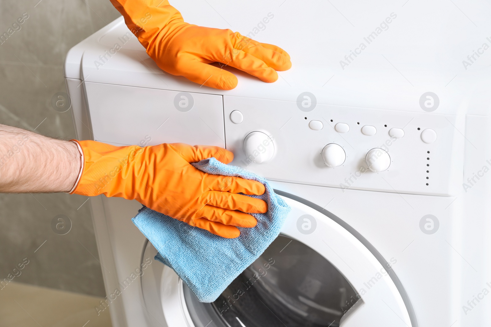 Photo of Man cleaning washing machine with rag indoors, closeup