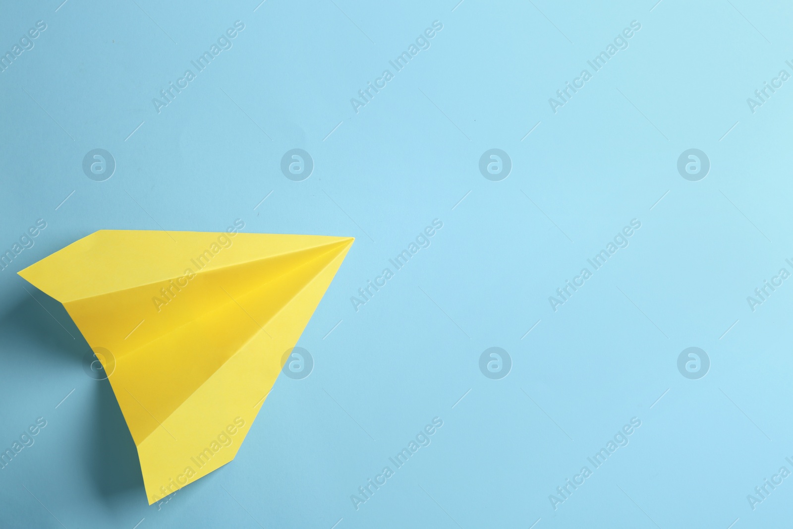 Photo of Yellow paper plane on light blue background, top view. Space for text