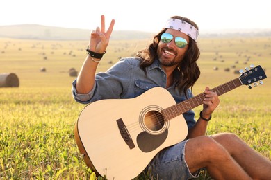 Happy hippie man with guitar showing peace sign in field