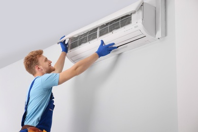 Professional technician maintaining modern air conditioner indoors