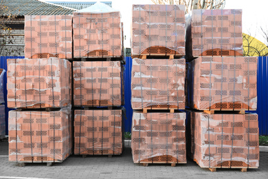 Photo of Pallets with red bricks outdoors. Building materials wholesale