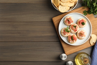 Delicious crackers with cream cheese, prosciutto and parsley on wooden table, flat lay. Space for text