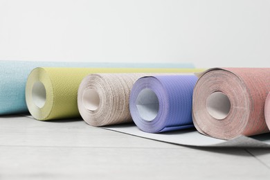 Image of Colorful wallpaper rolls on light wooden floor, closeup