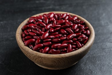 Photo of Raw red kidney beans in wooden bowl on black table, closeup
