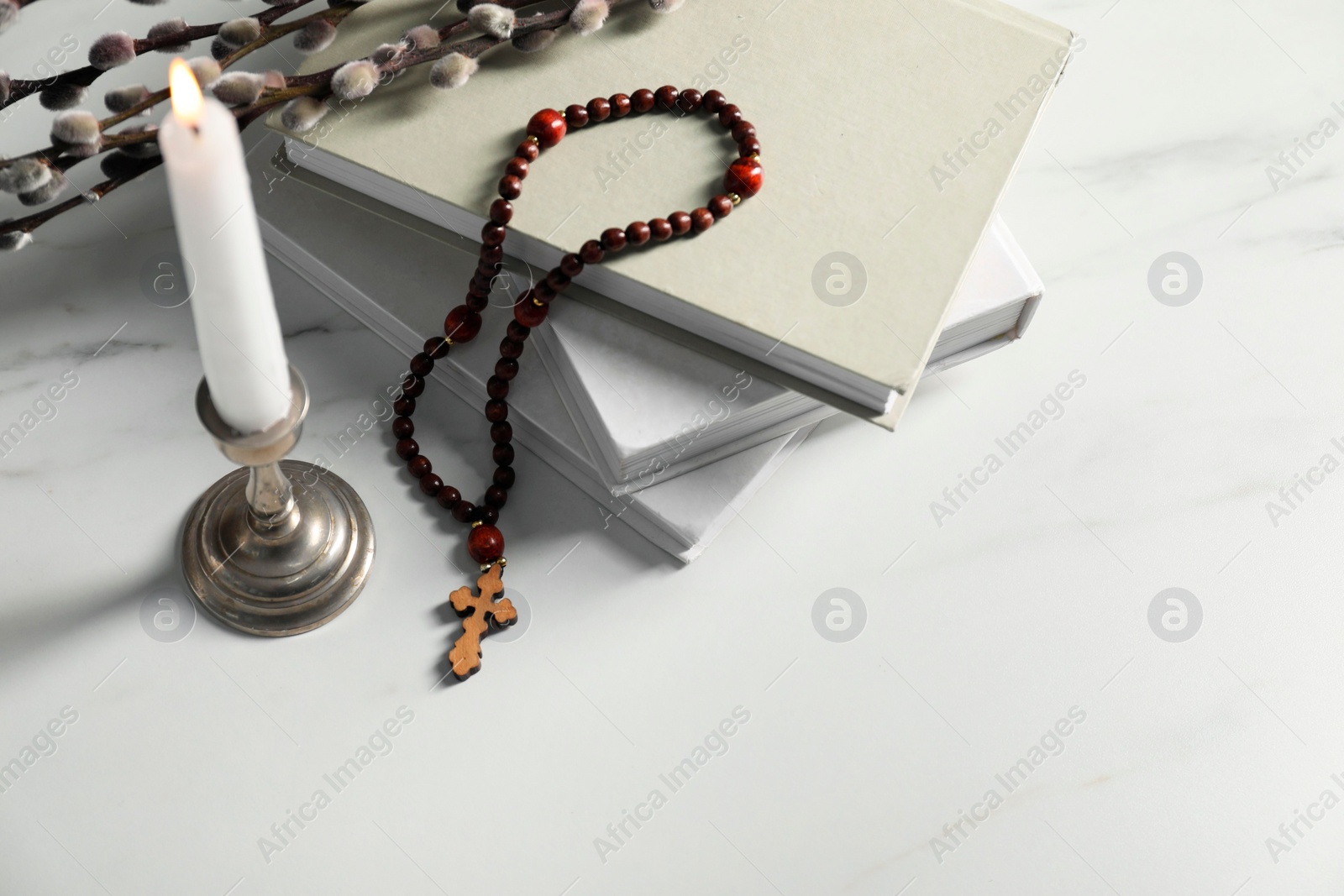 Photo of Books, burning candle, willow branches and rosary beads on white marble table, space for text