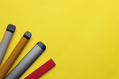 Different electronic cigarettes on yellow background, flat lay. Space for text