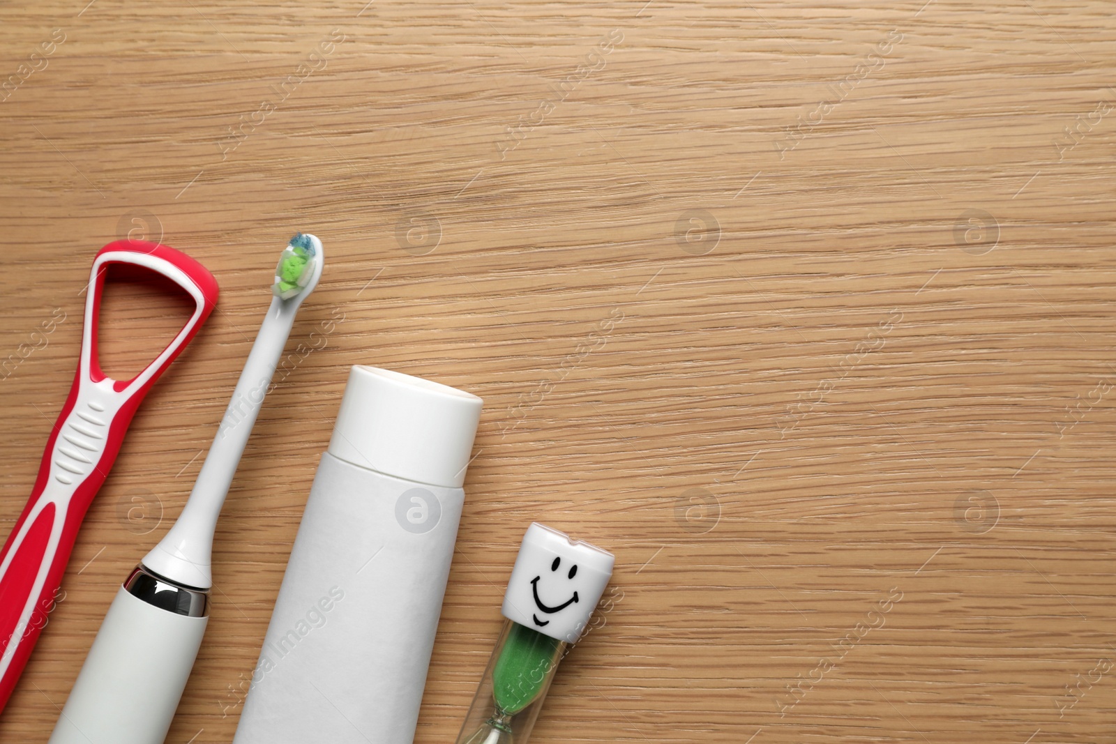 Photo of Tongue cleaner, toothbrush, paste and hourglass on wooden table, flat lay. Space for text