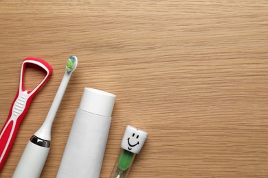 Tongue cleaner, toothbrush, paste and hourglass on wooden table, flat lay. Space for text