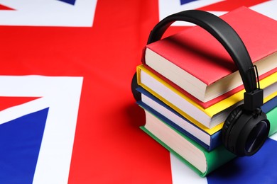 Photo of Learning foreign language. Different books and headphones on flag of United Kingdom, space for text