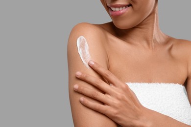 Photo of Young woman applying body cream onto arm on grey background, closeup. Space for text