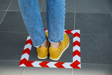 Photo of Woman standing on taped floor marking for social distance, closeup. Coronavirus pandemic